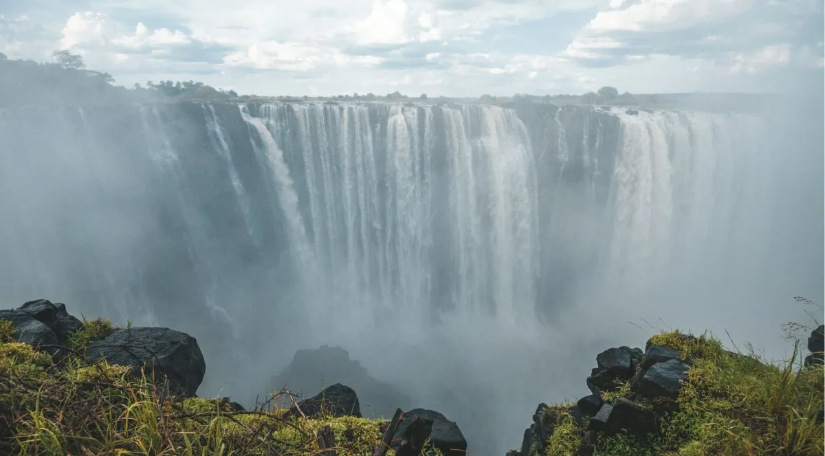 Wide panoramic view of Victoria Falls seen from the Zimbabwean rim, mist rising from the Batoka Gorge with dark storm clouds overhead
